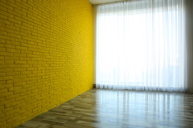 Photo of Empty room with yellow brick wall, large window and wooden floor
