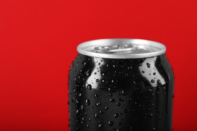 Photo of Black can of energy drink with water drops on red background, closeup
