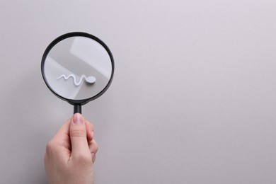 Photo of Reproductive medicine. Woman looking at sperm cell through magnifier on gray background, top view with space for text