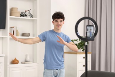 Photo of Smiling teenage blogger explaining something while streaming at home