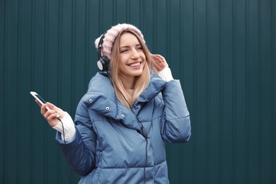 Young woman with headphones listening to music near color wall, outdoors