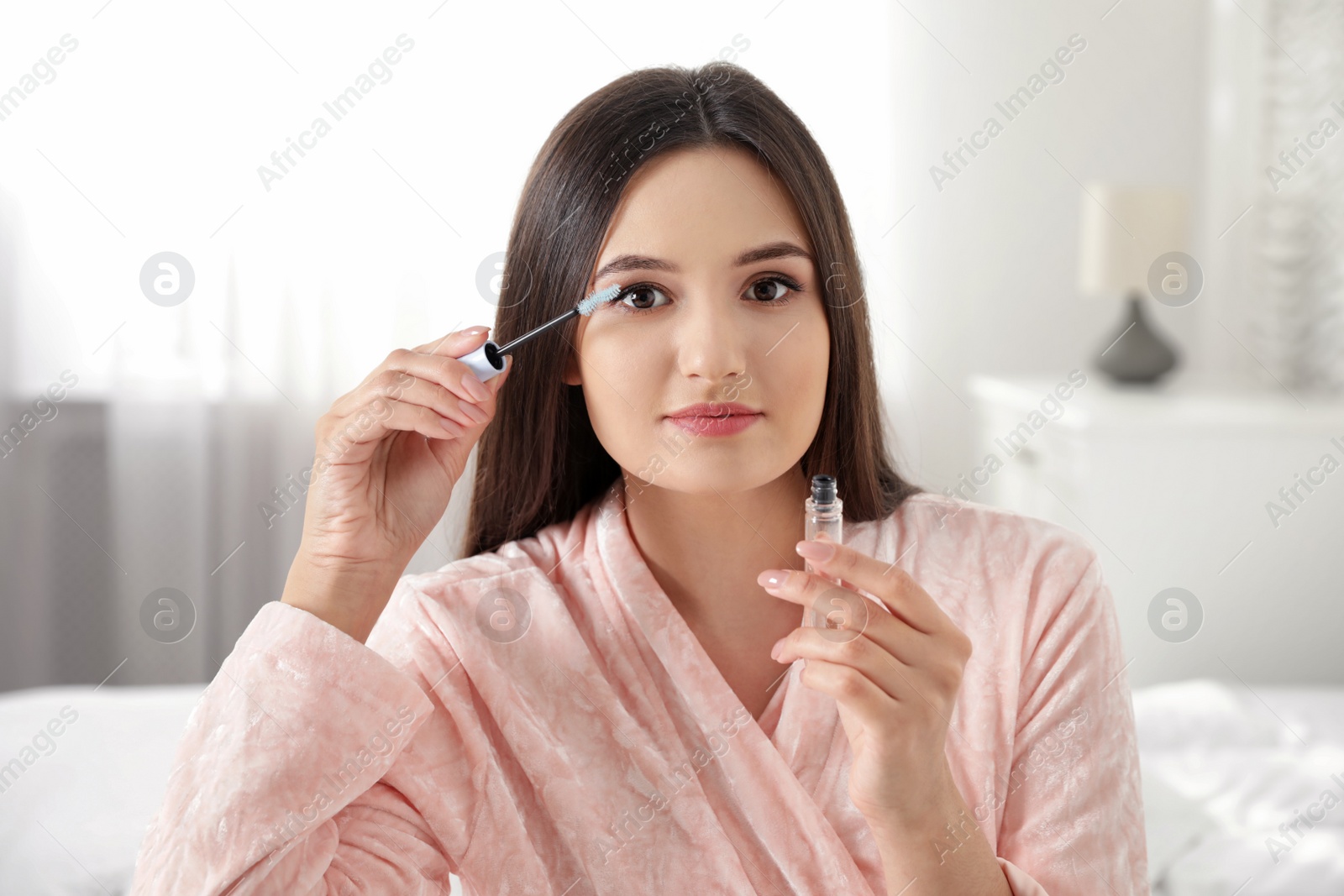 Photo of Beautiful woman applying oil onto her eyelashes indoors