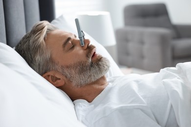 Photo of Man sleeping with clothespin on his nose in bed at home. Problem with snoring