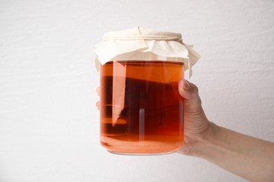 Photo of Woman holding glass jar of tasty kombucha on white background, closeup