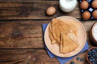 Photo of Delicious crepes and ingredients on wooden table, flat lay. Space for text