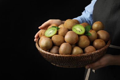 Photo of Woman holding wicker bowl with fresh ripe kiwis on black background, closeup