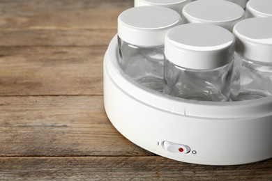 Photo of Modern yogurt maker with empty jars on wooden table, closeup. Space for text