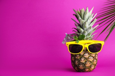 Photo of Fresh pineapple with sunglasses, umbrella and mint as summer cocktail on color background, space for text