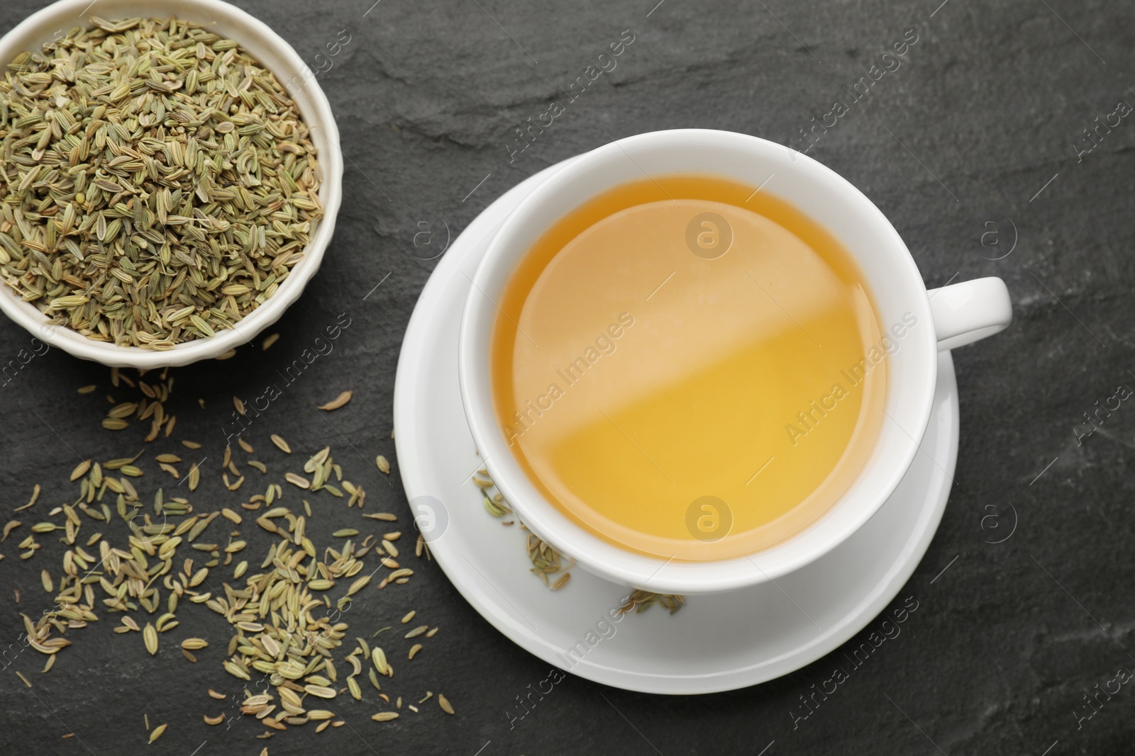 Photo of Aromatic fennel tea in cup and seeds on black table, flat lay