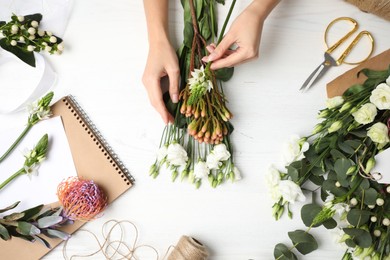 Photo of Florist making beautiful bouquet at white wooden table, top view