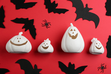 Image of White pumpkin shaped candle holders with decorative bats and spiders on red background, flat lay. Halloween celebration