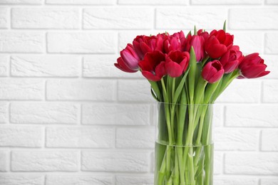 Photo of Bouquet of beautiful tulips in glass vase near white brick wall. Space for text