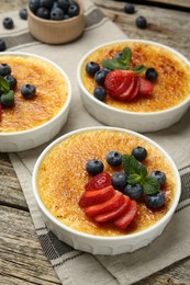 Photo of Delicious creme brulee with berries and mint in bowls on wooden table