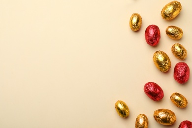 Photo of Chocolate eggs wrapped in red and golden foil on beige background, flat lay. Space for text