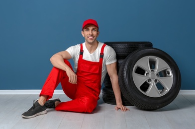 Photo of Young mechanic sitting near car tires near color wall