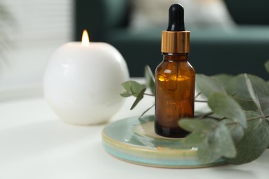 Photo of Aromatherapy. Bottle of essential oil, burning candle and eucalyptus leaves on white table