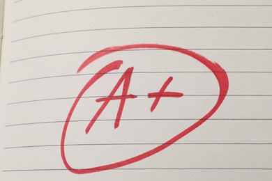 Photo of School grade. Red letter A with plus symbol on notebook paper, top view