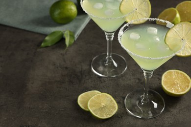 Photo of Delicious Margarita cocktail with ice cubes in glasses and limes on grey table, space for text
