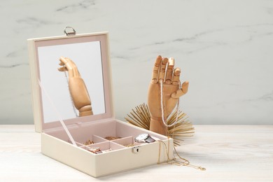 Photo of Jewelry box with many different accessories and mannequin hand on white wooden table. Space for text