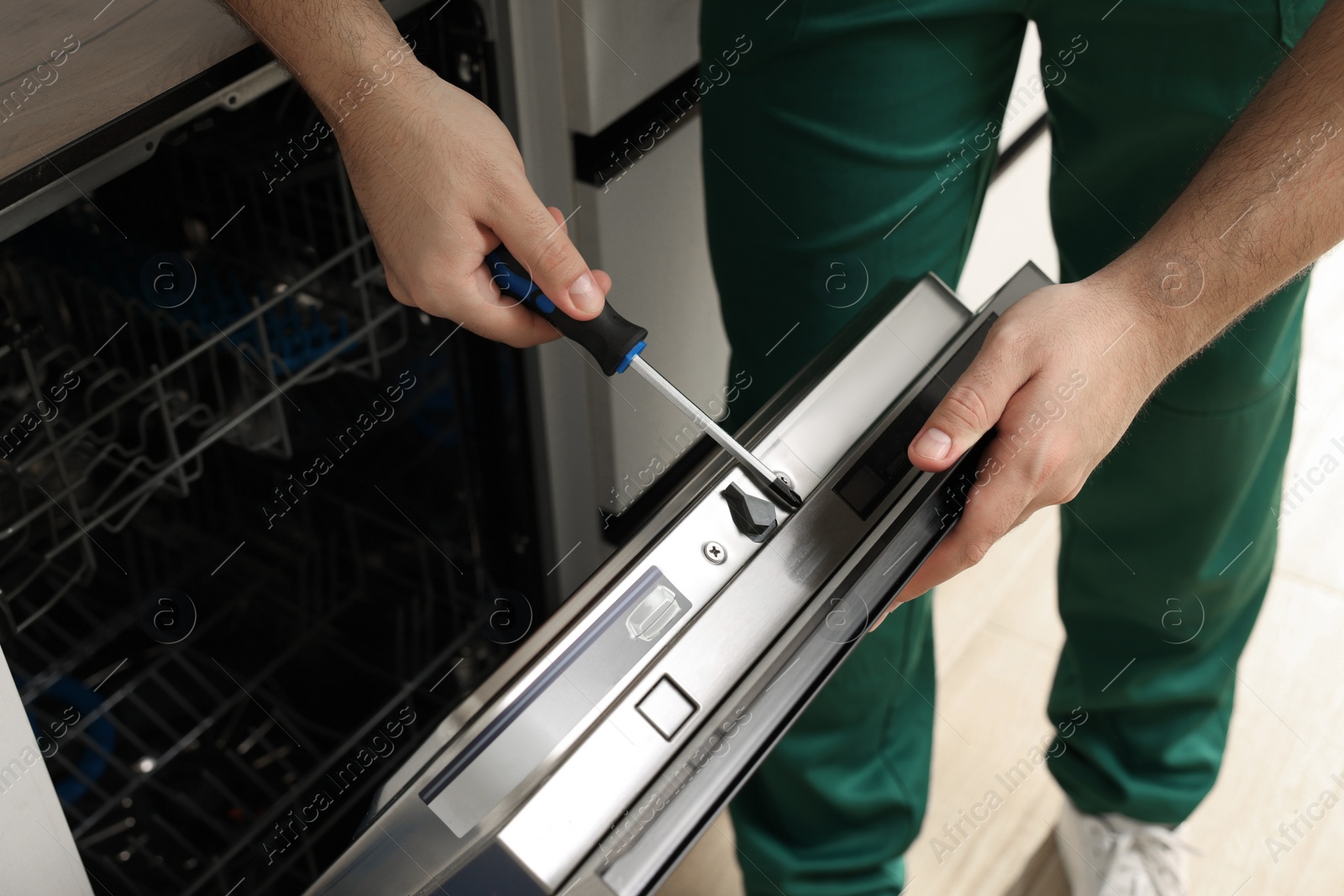 Photo of Serviceman repairing dishwasher door with screwdriver indoors, closeup