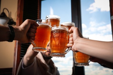 Photo of Friends clinking glasses with beer in pub, closeup
