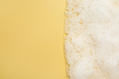 Photo of White washing foam on yellow background, top view. Space for text