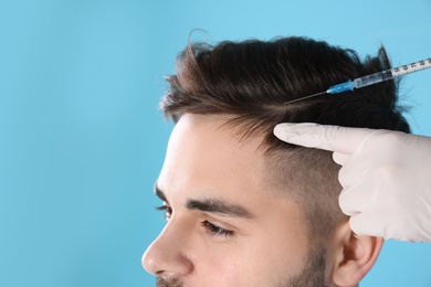 Photo of Young man with hair loss problem receiving injection on color background, closeup