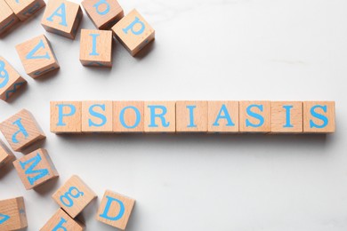 Photo of Word Psoriasis made of wooden cubes with letters on white table, flat lay