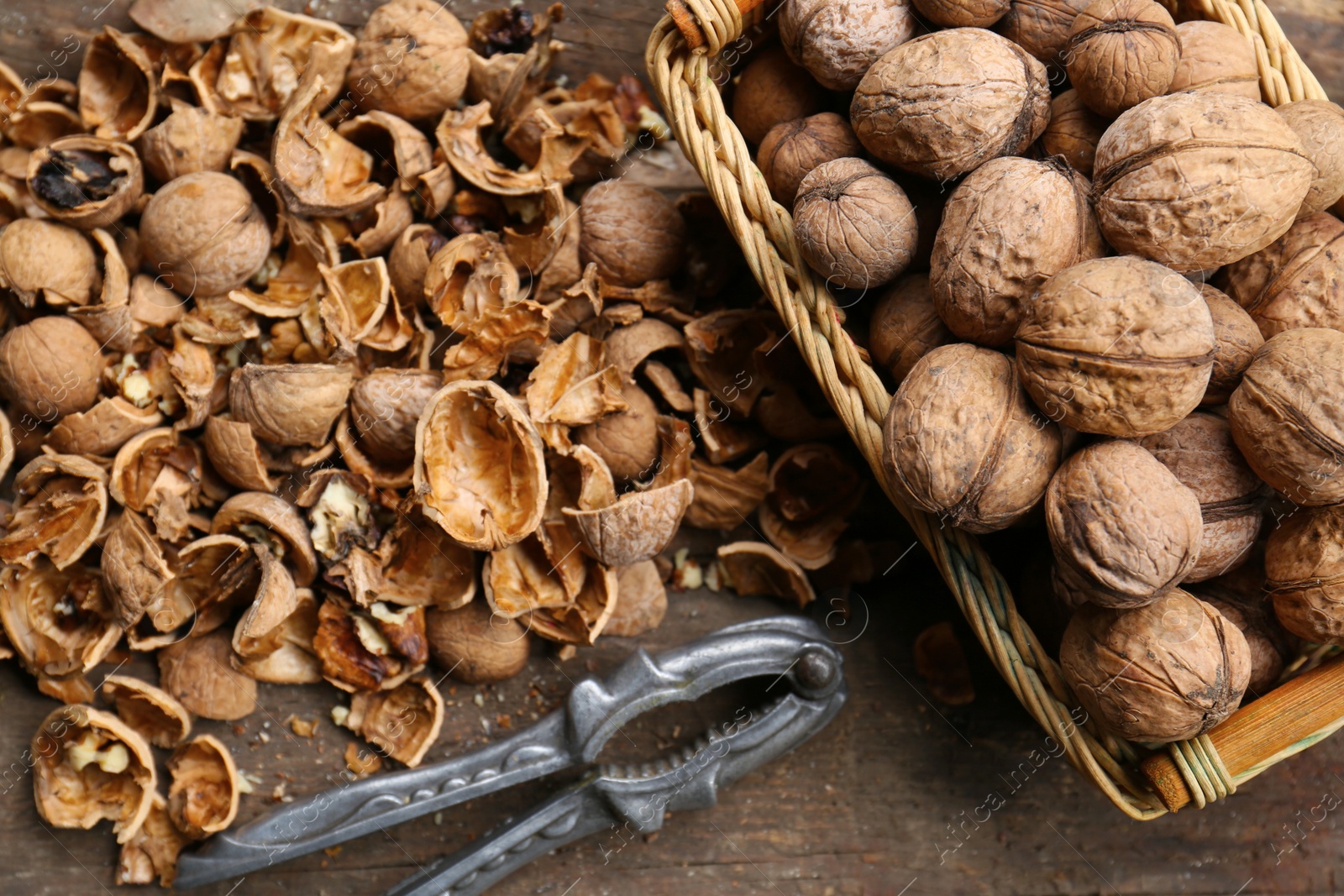 Photo of Walnuts, pieces of shells and nutcracker on wooden table, flat lay