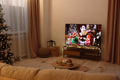 Photo of Wide TV set, furniture, snacks and Christmas tree in stylish room