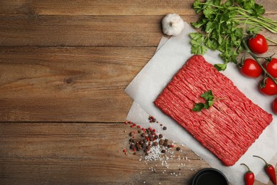 Photo of Raw fresh minced meat, tomatoes and other ingredients on wooden table, flat lay. Space for text