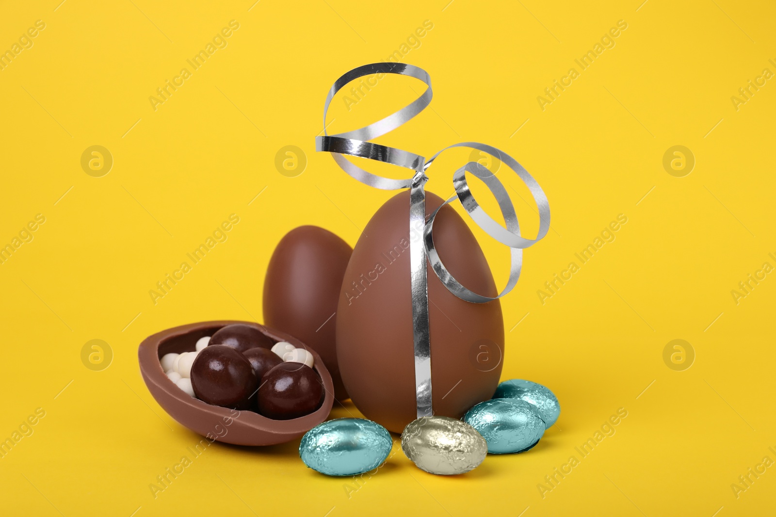 Delicious chocolate eggs and candies on yellow background, closeup Photo of Delicious chocolate eggs and candies on yellow background, closeup