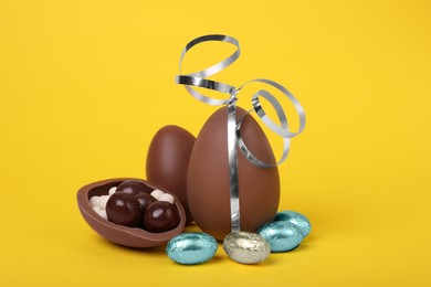 Photo of Delicious chocolate eggs and candies on yellow background, closeup