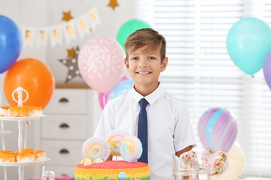 Photo of Happy boy at table with treats in room decorated for birthday party