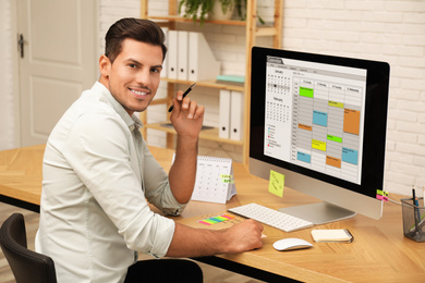 Photo of Handsome man using calendar app on computer in office