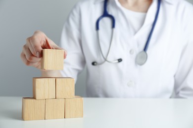 Photo of Doctor building pyramid of blank wooden cubes on white table against grey background, closeup. Space for text