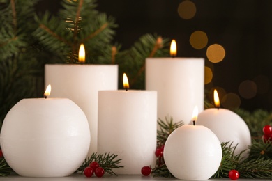 Photo of Burning white candles with fir tree branches on table against blurred Christmas lights