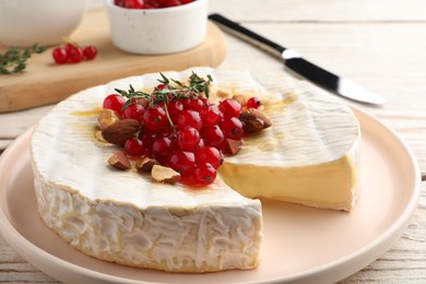 Photo of Brie cheese served with almonds, red currants and honey on white wooden table, closeup