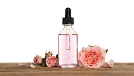 Photo of Bottle of rose essential oil and flowers on table, white background