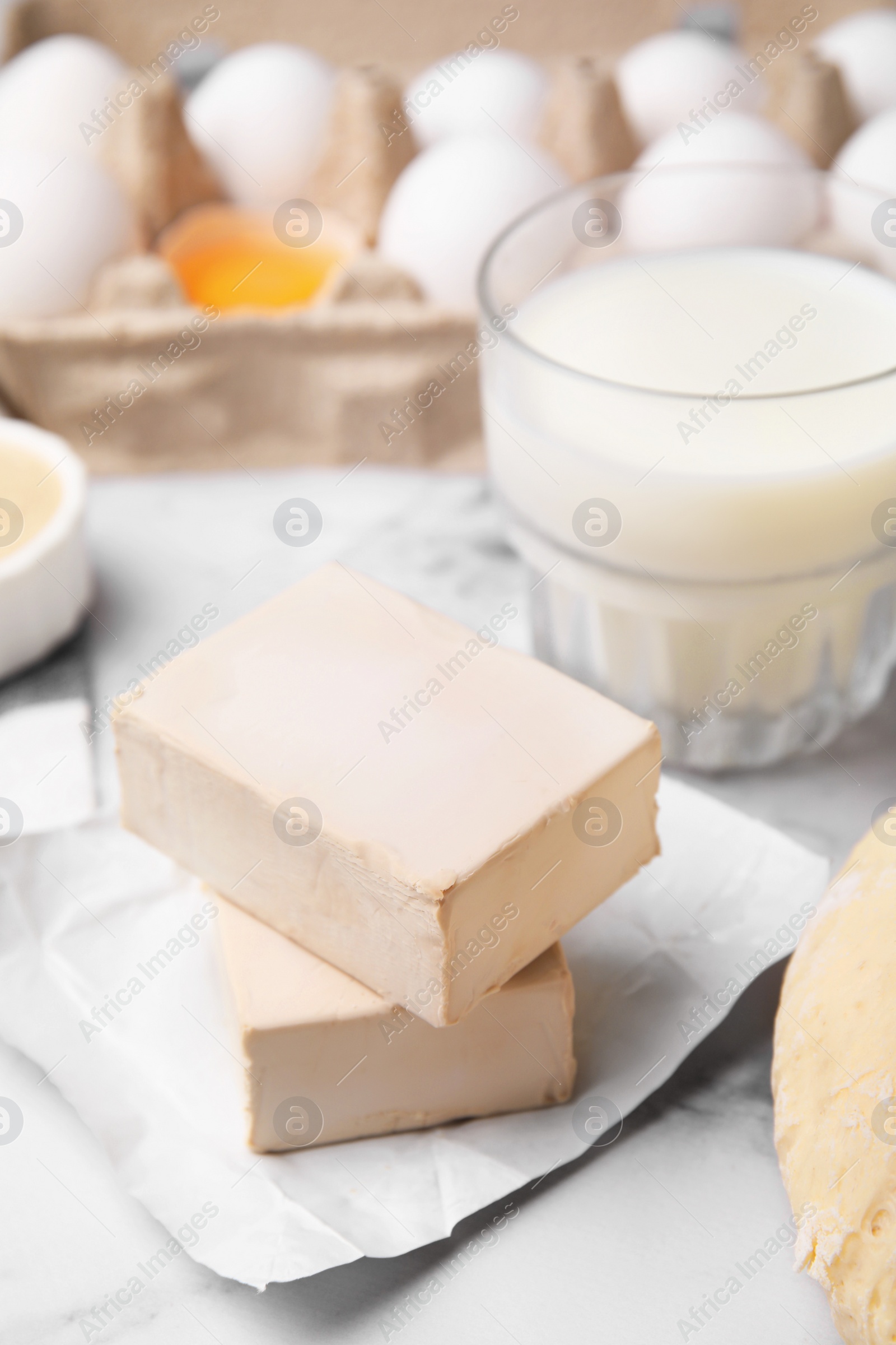 Photo of Blocks of compressed yeast and ingredients on white marble table, closeup