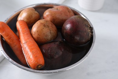 Photo of Fresh vegetables with water for vinaigrette salad in bowl on white table, closeup.