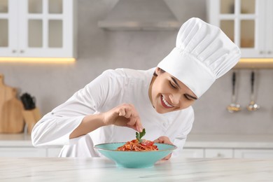 Photo of Professional chef decorating delicious spaghetti with parsley at marble table in kitchen