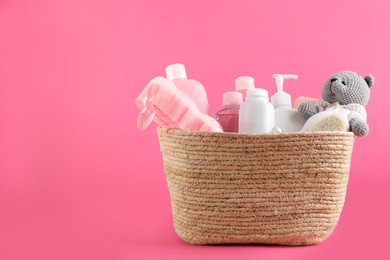 Photo of Different baby cosmetic products, bathing accessories and toy in wicker basket on pink background. Space for text