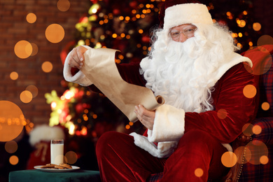 Photo of Santa Claus with wish list near Christmas tree indoors