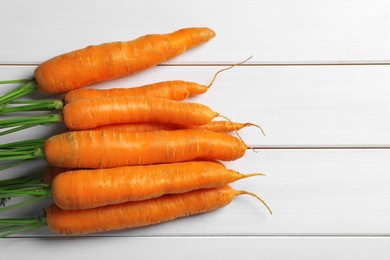 Photo of Many tasty ripe carrots on white wooden table, flat lay. Space for text
