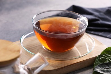 Photo of Aromatic hot tea in glass cup and leaves on light grey table, closeup