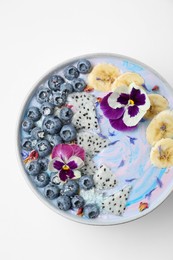 Photo of Delicious smoothie bowl with fresh fruits, blueberries and flowers on white background, top view