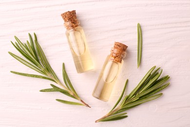 Photo of Essential oil in bottles and rosemary on white wooden table, flat lay