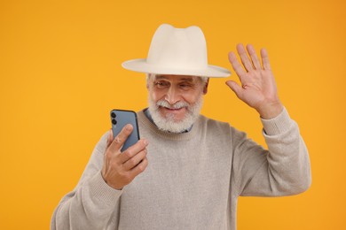 Photo of Happy senior man with smartphone having video chat on yellow background