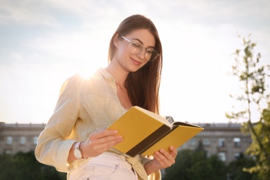 Photo of Young woman reading book outdoors on sunny day